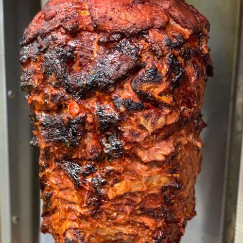 A vertical skewer of roasted meat with a crispy, charred exterior, ready to be sliced for serving.
