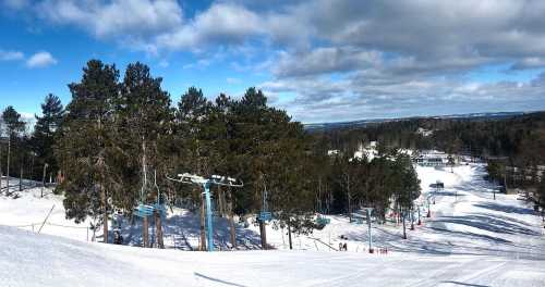 A snowy ski slope with trees, ski lifts, and a clear blue sky in the background.