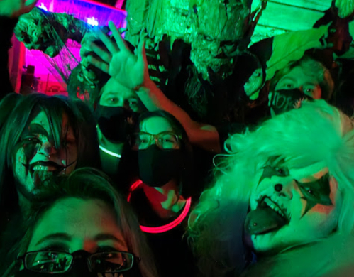A group of people in Halloween costumes, wearing masks and face paint, posing in a colorful, spooky setting.