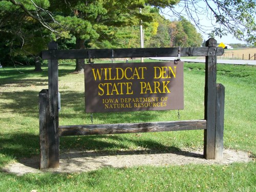Sign for Wildcat Den State Park, Iowa Department of Natural Resources, surrounded by trees and grass.