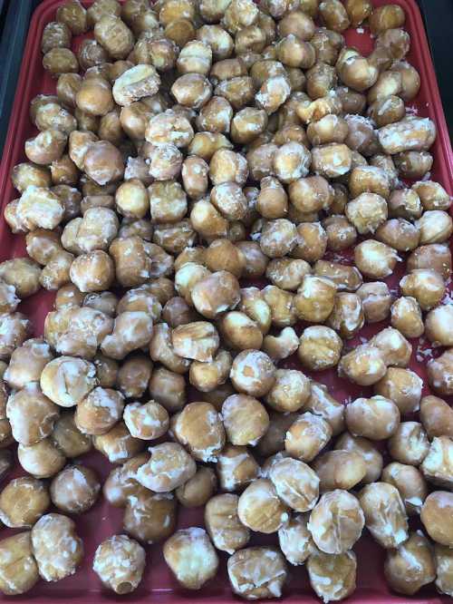 A tray filled with small, round, glazed doughnut holes, golden brown and coated in a sugary glaze.