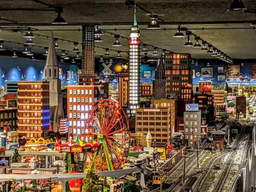 A detailed miniature cityscape featuring buildings, a Ferris wheel, and train tracks under dim lighting.