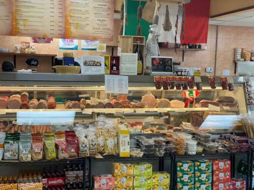 A deli display featuring various meats, cheeses, and packaged goods, with a menu board above.