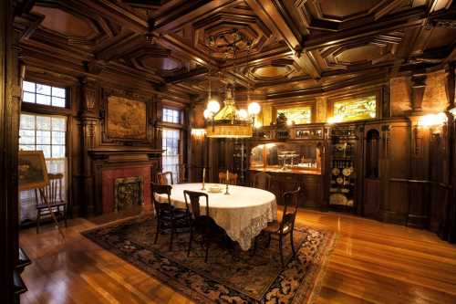 A richly decorated dining room with wooden paneling, a round table, and vintage lighting fixtures.