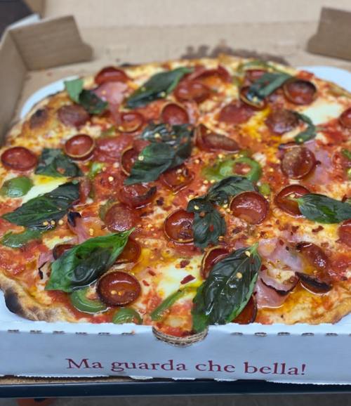 A delicious pizza topped with pepperoni, basil, and mozzarella, presented in a pizza box with Italian text.
