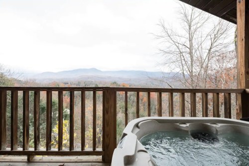 A hot tub on a wooden deck overlooks a misty mountain landscape with autumn foliage.