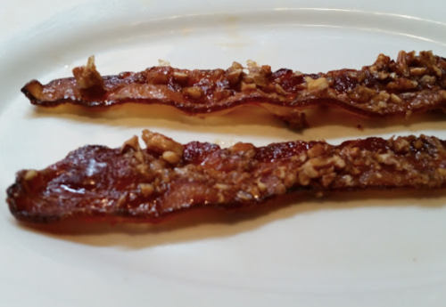 Two strips of crispy bacon topped with a crunchy, nutty coating on a white plate.