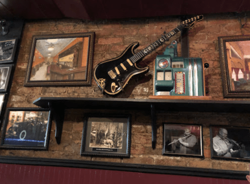 A wall display featuring a guitar, vintage jukebox, and framed black-and-white photos in a cozy bar setting.