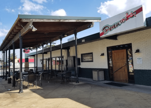 Exterior of Dean's restaurant featuring a covered patio and outdoor seating area. Bright blue sky in the background.