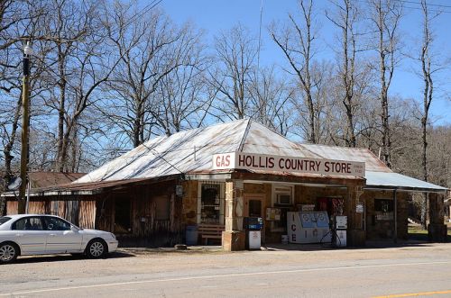 A rustic country store with a gas station sign, surrounded by bare trees and a parked car in front.
