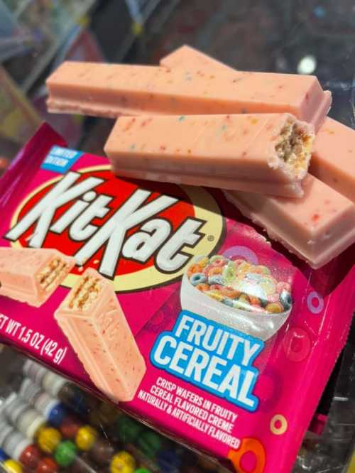 A box of Fruity Cereal KitKat bars with a few bars resting on top, showcasing their pink color and crispy texture.