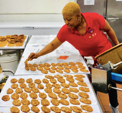 A woman in a red shirt arranges freshly baked cookies on a table in a kitchen.