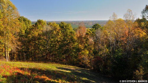 A scenic view of a colorful autumn landscape with trees and rolling hills under a clear blue sky.