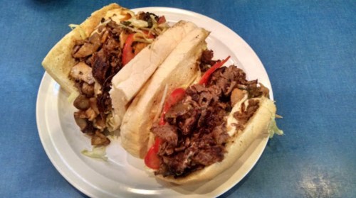 Two hearty sandwiches filled with sliced meats, peppers, and lettuce on a white plate, set against a blue background.