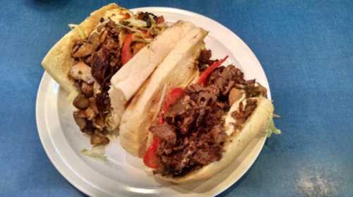 Two hearty sandwiches filled with sliced meats, peppers, and lettuce on a white plate, set against a blue background.