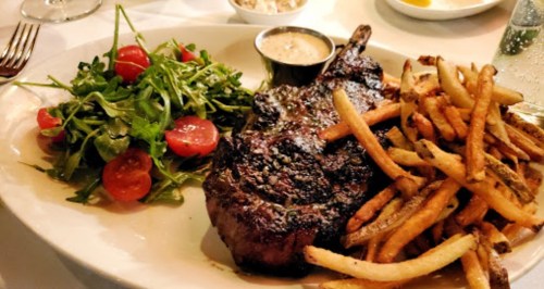 A plate featuring a grilled steak, crispy fries, and a side salad with cherry tomatoes.