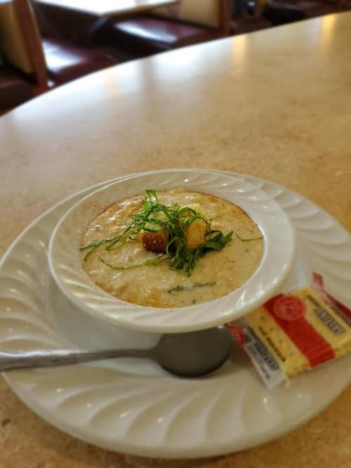A bowl of creamy soup topped with herbs and croutons, served with a packet of crackers on a table.