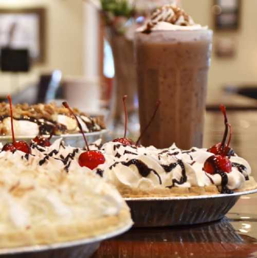 Two dessert pies topped with whipped cream and cherries, alongside a chocolate milkshake with whipped cream.