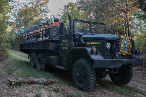 A large black truck with passengers, parked on a dirt path surrounded by trees, labeled "Zombie Paintball Patrol."