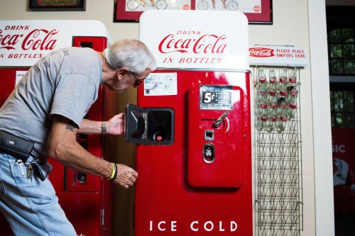An older man inspects a vintage Coca-Cola vending machine in a nostalgic setting.
