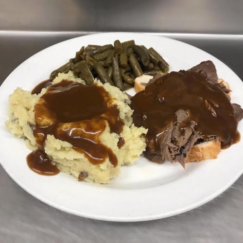 A plate with mashed potatoes topped with gravy, green beans, and slices of roast beef with brown sauce.