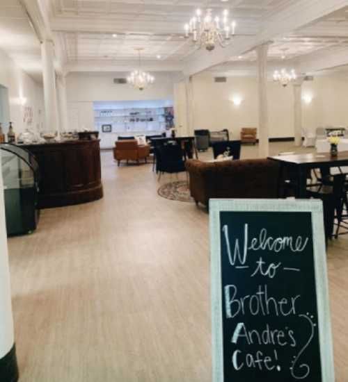 A spacious café interior with seating areas and a welcome sign for Brother Andre's Café.