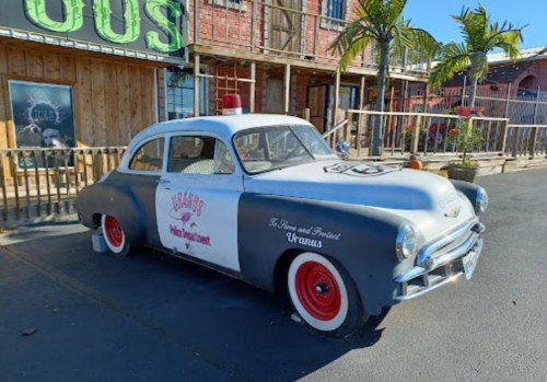 A vintage police car with a two-tone paint job parked outside a building, featuring a red light on top.