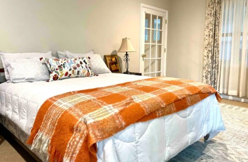 Cozy bedroom featuring a large bed with an orange plaid blanket, decorative pillows, and soft lighting.