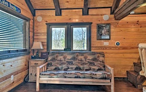 Cozy interior of a cabin with a wooden sofa, large windows, and rustic decor, featuring a nature-themed print.