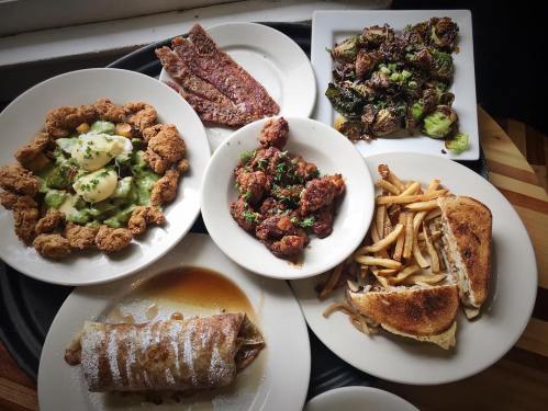 A variety of dishes on a tray, including fried chicken, salad, fries, and a dessert roll.