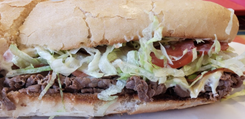 A close-up of a sandwich filled with sliced beef, lettuce, tomatoes, and mayonnaise on a crusty bread roll.