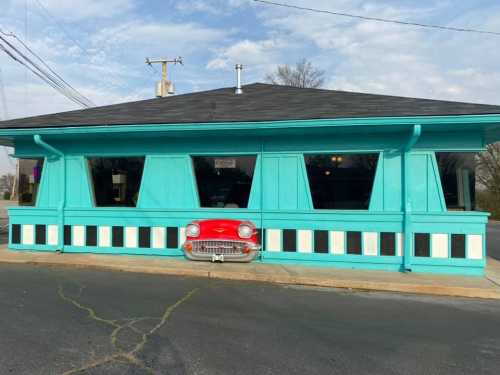 A turquoise restaurant with large windows and a red car front embedded in the wall, featuring black and white accents.