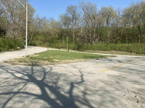 A winding road curves through a wooded area, with shadows cast on the pavement from nearby trees.