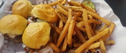 A basket of three mini burgers with pulled meat and a side of crispy French fries.