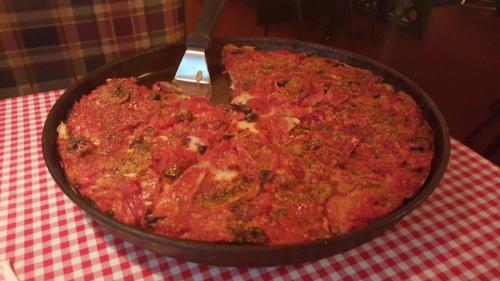 A deep-dish pizza with a thick layer of tomato sauce and toppings, served in a round pan on a checkered tablecloth.