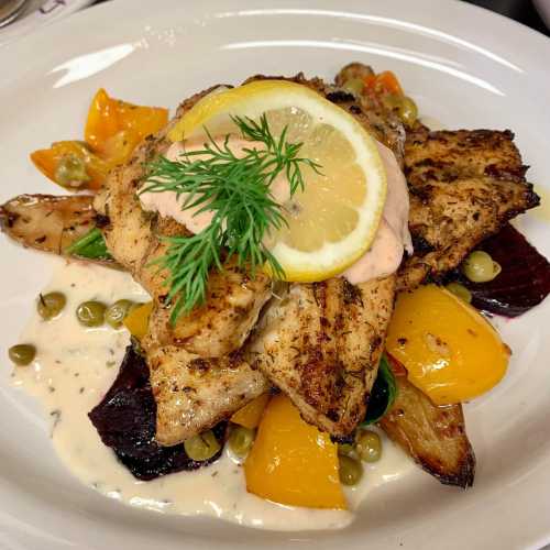 Grilled fish topped with lemon and dill, served on a bed of colorful roasted vegetables and creamy sauce.