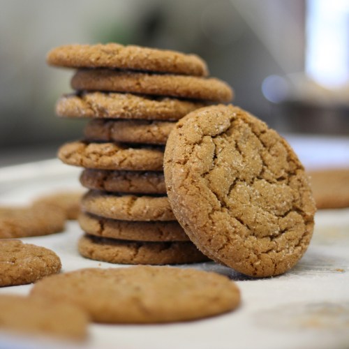 A stack of freshly baked cookies on a baking sheet, with some cookies scattered around.
