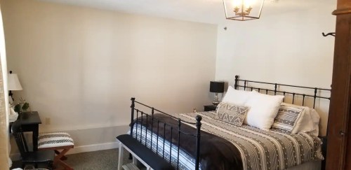 Cozy bedroom featuring a black metal bed, patterned bedding, a small desk, and a warm light fixture.