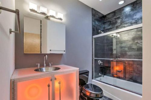 Modern bathroom featuring a sleek design with a glass shower, illuminated sink cabinet, and dark tile accents.