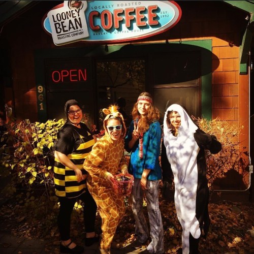 A group of five people in fun costumes stand outside a coffee shop, surrounded by autumn leaves.