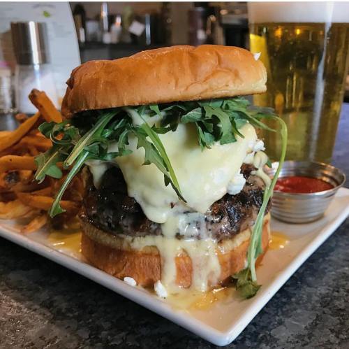 A juicy burger topped with melted cheese and arugula, served with fries and a beer in the background.