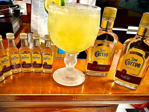 A large margarita in a glass with lime, surrounded by mini and regular bottles of Jose Cuervo tequila.