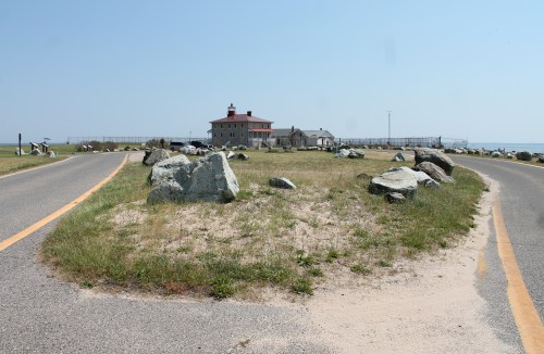 A fork in the road leads to a historic building surrounded by grass and rocks, with a clear blue sky above.