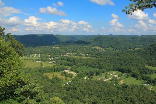 A panoramic view of lush green hills and valleys under a blue sky with fluffy clouds.