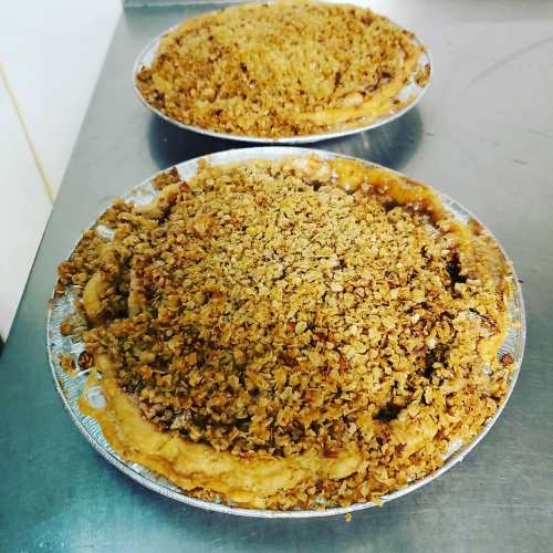 Two freshly baked pies with golden, crumbly topping on a silver surface.