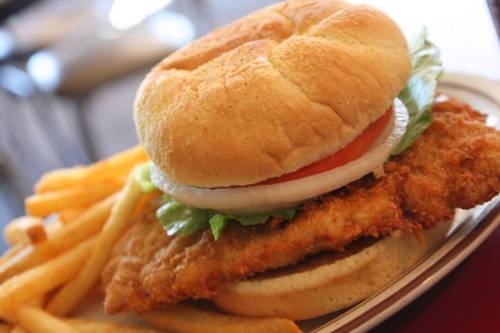 A crispy fried chicken sandwich with lettuce, tomato, and onion, served with a side of golden French fries.