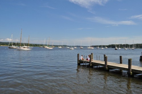 A serene waterfront scene with sailboats on calm water and a wooden dock under a clear blue sky.