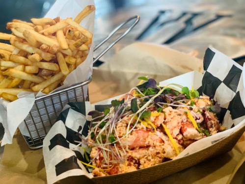 A plate of colorful seafood salad topped with microgreens, served with a side of crispy French fries in a basket.