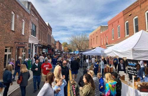 A bustling street market with crowds of people, food stalls, and shops under a blue sky with scattered clouds.