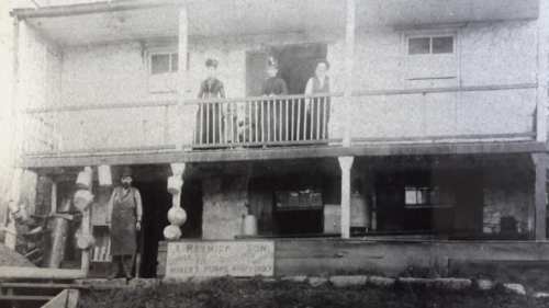 Historic black-and-white photo of a two-story building with people on the balcony and a sign in front.